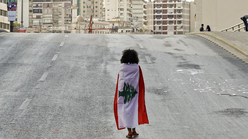 TOPSHOT - A Lebanese woman protester walks draped in a national flag along the Fuad Chehab avenue, near the Martyrs' Square, in the centre of the capital Beirut on October 29, 2019 on the 13th day of anti-government protests. - An unprecedented cross-sectarian movement has brought major cities across Lebanon to a standstill since October 17, as protesters keep up demands for a complete overhaul of the political system. (Photo by JOSEPH EID / AFP) (Photo by JOSEPH EID/AFP via Getty Images)
