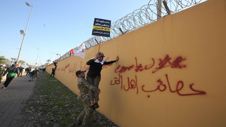 A member of an Iraqi Shiite paramilitary group helps a fellow protesters holding a placard denouncing the United States climb on the outer wall of the US embassy in Baghdad's Green Zone during an angry demonstration on December 31, 2019 to denounce weekend US air strikes that killed Iran-backed fighters in Iraq. Arabic graffiti reads: "Assaib Ahl al-Haq" -- a pro-Iran Iraqi Shiite group whose leaders were recently hit with US sanctions. - It was the first time in years protesters have been able to reach the