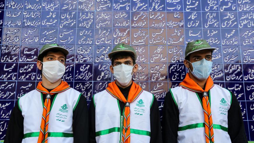 TOPSHOT - Members of a student organisation, mask-clad due to the COVID-19 coronavirus pandemic, stand before a wall showing the names of donors at Nojavanan school in Iran's capital Tehran on the first day of schools re-opening on September 5, 2020. (Photo by ATTA KENARE / AFP) (Photo by ATTA KENARE/AFP via Getty Images)