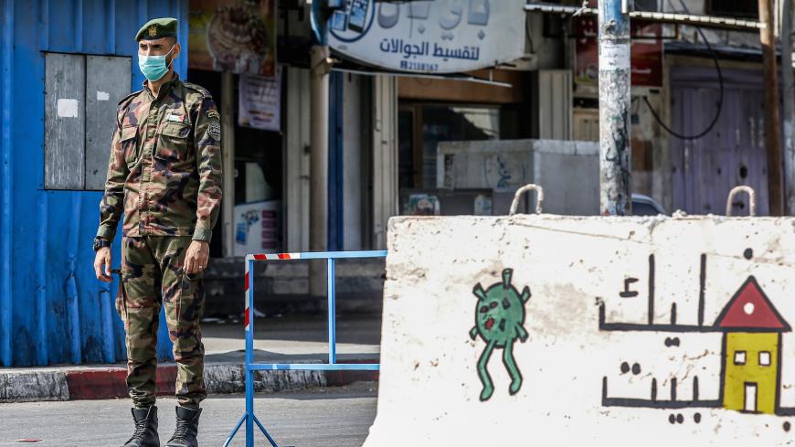 A mask-clad policeman loyal to Hamas stands behind concrete barriers painted with messages instructing people to remain at home due to the COVID-19 coronavirus pandemic at a checkpoint in Rafah in the southern Gaza Strip on September 6, 2020. (Photo by SAID KHATIB / AFP) (Photo by SAID KHATIB/AFP via Getty Images)