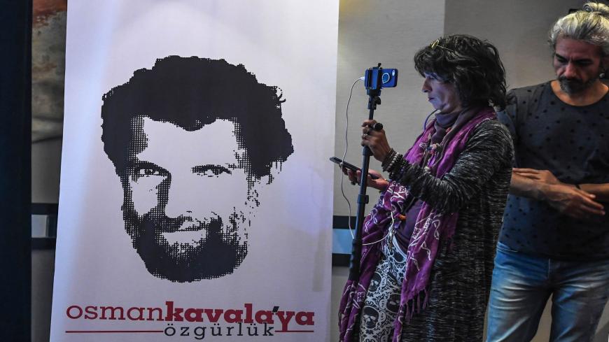 A journalist stands in front of a poster featuring jailed businessman and philanthropist Osman Kavala during a press conference of his lawyers on October 31, 2018. - Osman Kavala was arrested a year ago by Turkish authorities and has still to be charged with an offence. (Photo by OZAN KOSE / AFP)        (Photo credit should read OZAN KOSE/AFP via Getty Images)