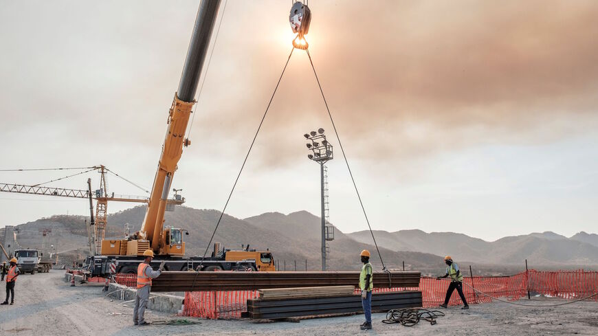 Workers move iron girders from a crane at the Grand Ethiopian Renaissance Dam (GERD), near Guba in Ethiopia, on December 26, 2019. - The Grand Ethiopian Renaissance Dam, a 145-metre-high, 1.8-kilometre-long concrete colossus is set to become the largest hydropower plant in Africa.
Across Ethiopia, poor farmers and rich businessmen alike eagerly await the more than 6,000 megawatts of electricity officials say it will ultimately provide. 
Yet as thousands of workers toil day and night to finish the project, E