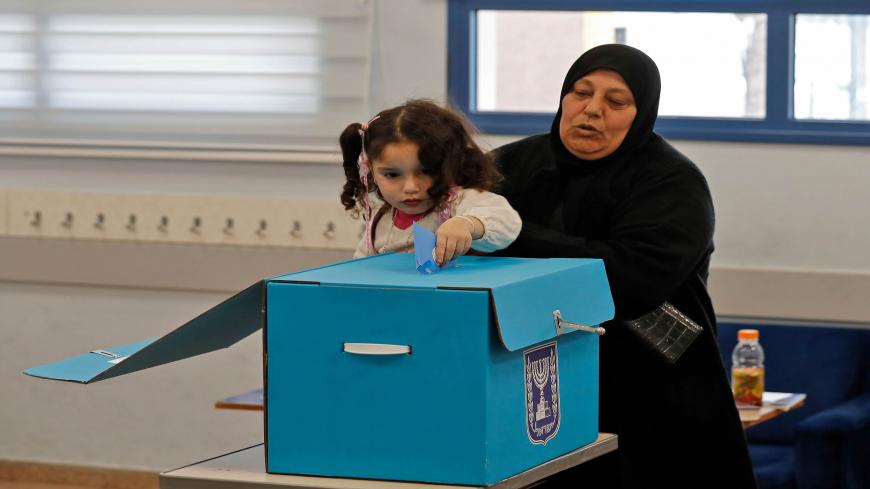 An Arab Israeli woman holds a child casting her vote in a ballot box during the country's parliamentary elections at a polling station in the Arab city of Tamra in northern Israel on March 2, 2020. - Israelis were voting for a third time in 12 months today, with embattled Prime Minister Benjamin Netanyahu seeking to end the country's political crisis and save his career. (Photo by Ahmad GHARABLI / AFP) (Photo by AHMAD GHARABLI/AFP via Getty Images)