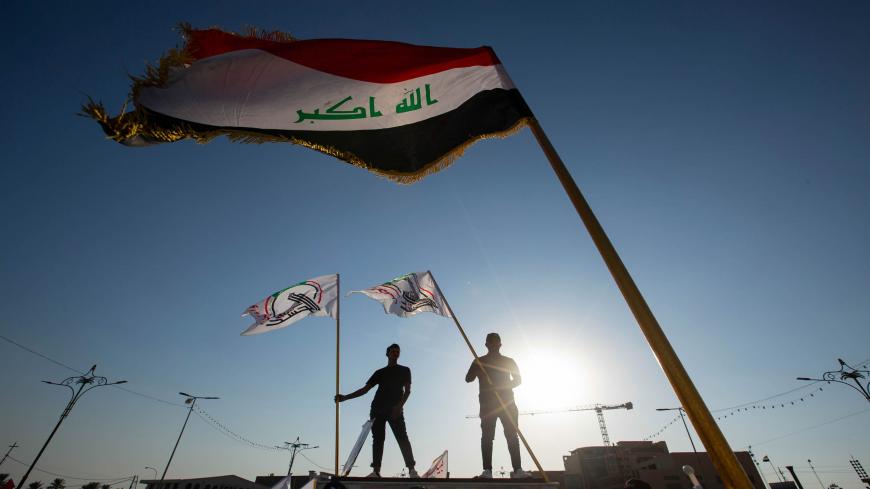 Supporters of Hashed al-Shaabi, an Iraqi paramilitary network dominated by Iran-backed factions, wave the Hashed flag as they stand under the national flag during a protest denouncing comments made by Kurdish ex-minister and to show their support to the paramilitary network in the southern Iraqi city of Basra on October 17, 2020. - Hashed supporters burned down the main Kurdish party's headquarters in Baghdad after criticism from a Iraq's Former Foreign Minister Hoshyar Zebari. Hundreds of Hashed demonstrat
