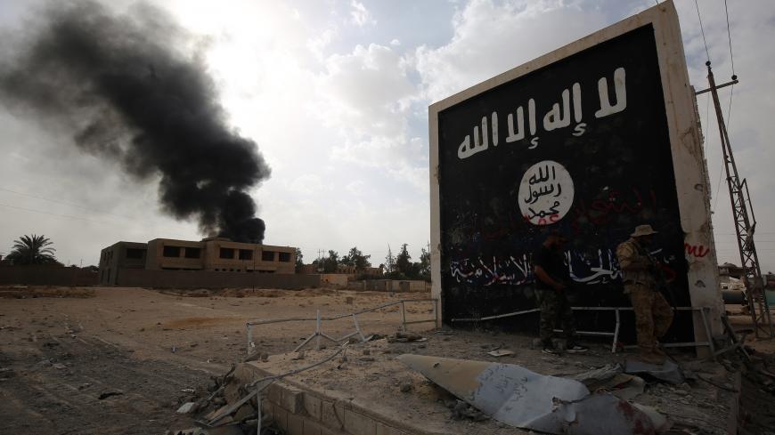 Iraqi fighters of the Hashed al-Shaabi (Popular Mobilisation units) stand next to a wall bearing the Islamic State (IS) group flag as they enter the city of al-Qaim, in Iraq's western Anbar province near the Syrian border as they fight against remnant pockets of Islamic State group jihadists on November 3, 2017.  / AFP PHOTO / AHMAD AL-RUBAYE        (Photo credit should read AHMAD AL-RUBAYE/AFP via Getty Images)