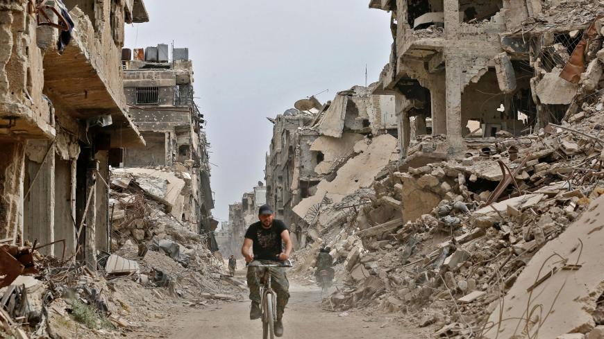 A member of the Syrian pro-government forces rides a bicycle through a damaged street in the Yarmuk Palestinian refugee camp on the southern outskirts of the capital Damascus on May 22, 2018. - The government seized earlier in the week the Yarmuk Palestinian camp and adjacent neighbourhoods of Tadamun and Hajar al-Aswad from the Islamic State (IS) group , putting Damascus fully under its control for the first time since 2012. (Photo by LOUAI BESHARA / AFP) / The erroneous mention[s] appearing in the metadat