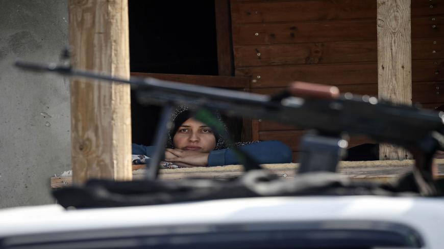 A Palestinian woman watches from her home's window fighters from the Ezz-Al Din Al-Qassam Brigades, the armed wing of the Hamas movement, taking part in an anti-Israel military show in Khan Yunis in the southern Gaza Strip November 11, 2019 to mark one year since their comrade Nour Baraka, a commander in the group, was killed in an Israeli military operation in the Gaza Strip. (Photo by SAID KHATIB / AFP) (Photo by SAID KHATIB/AFP via Getty Images)