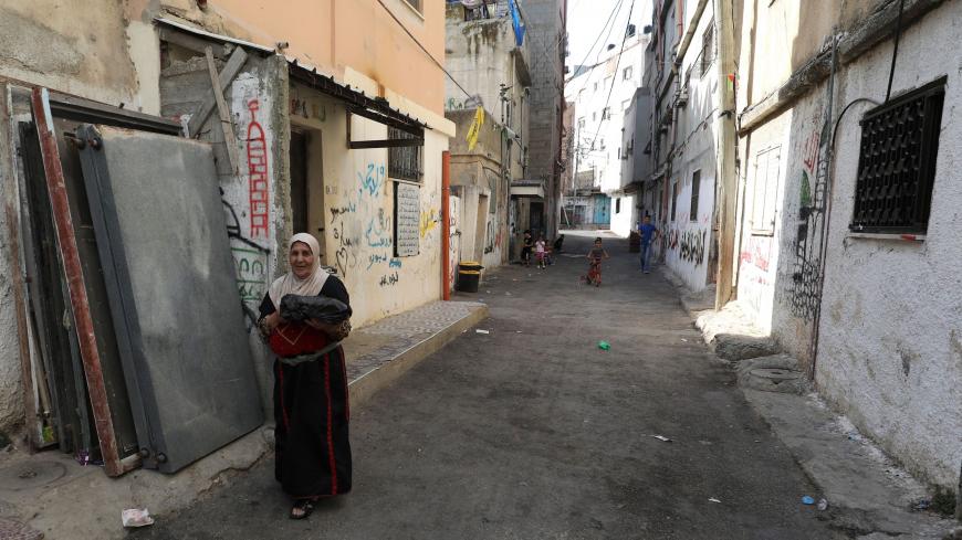 A Palestinian woman walks down a street in the Amari refugee camp near the West Bank city of Ramallah on July 29, 2020. - A second wave of coronavirus infections sweeping the Israeli-occupied West Bank is fuelling fears of a surge in overcrowded Palestinian refugee camps where social distancing is widely seen as impossible. The Palestinian health ministry's Tuesday update logged more than 10,860 confirmed cases of infection since the start of the pandemic, including more than 75 deaths. (Photo by ABBAS MOMA