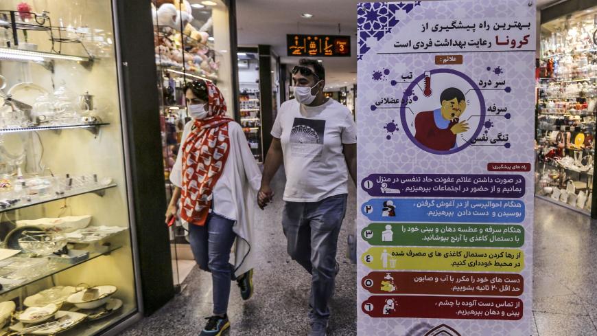 Iranians walk next to a sign advising people to wear masks as they shop in Tajrish square in the capital Tehran on November 1, 2020, amid the novel coronavirus pandemic crisis. - Iran yesterday announced the expansion beyond Tehran of measures against Covid-19, amid growing calls for a full lockdown after the country posted a string of record highs in deaths and infections. (Photo by ATTA KENARE / AFP) (Photo by ATTA KENARE/AFP via Getty Images)