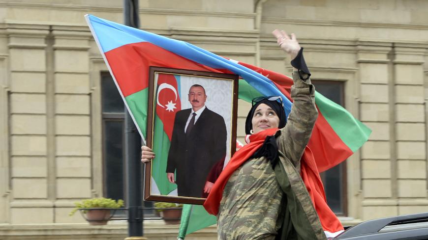A woman holds the national flag and a portrait of  Azerbaijan's President Ilham Aliyev as people celebrate in the streets of the capital Baku on November 10, 2020, after Armenia and Azerbaijan agreed a ceasefire following a string of Azeri victories in fighting over the disputed Nagorno-Karabakh region. - Armenia and Azerbaijan agreed on a deal with Russia to end weeks of fierce clashes over Nagorno-Karabakh on November 10, 2020, after a string of Azerbaijani victories in its fight to retake the disputed re