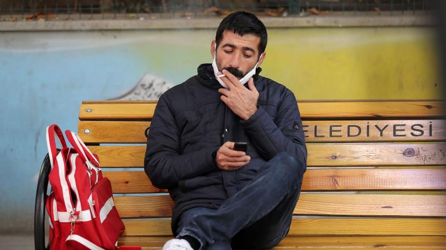 A man sitting on a public bench smokes a cigarette while using his  mobile phone in Ankara on November 13, 2020, after Turkey banned smoking in outdoor public areas as part of restrictions aimed at curbing the spread of the Covid-19 pandemic, caused by the novel coronavirus. - Turkey on November 11, 2020, announced a ban on smoking across the country in a number of outdoor spaces including crowded streets, public squares and transport stops, in a bid to limit rising Covid-19 infections. The ban was issued o