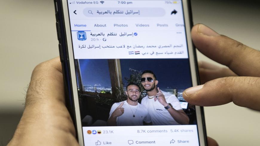 This picture taken on November 22, 2020 in Cairo shows a man holding a phone showing a picture of Egypt's self-proclaimed "superstar" Mohamed Ramadan posted by the official Facebook page of the State of Israel in Arabic (linked to the foreign ministry) depicting Ramadan (R) hugging Israeli midfielder Dia Saba in Dubai. - Ramadan, a 32-year-old actor and rapper, boasts millions of followers in the Arab world, is a close friend of Morocco's King Mohamed VI and the recipient of the 2019 All Africa Music Awards