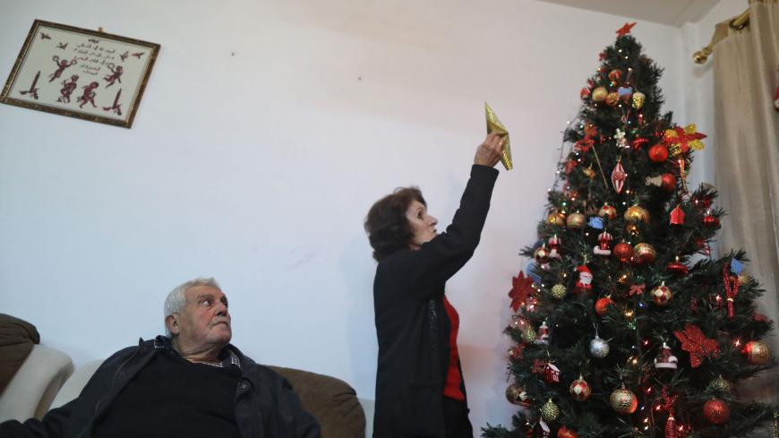 Nabil el-Salfiti looks on as his wife Faten (R) places the star on top of a Christmas tree at their home in Gaza City on December 22, 2019. - A few hundred Gazan Christians have traditionally been granted permits to attend Christmas festivities in Bethlehem and Jerusalem each year. This year Israel initially didn't announce any permits, prompting criticism among church groups and media. (Photo by MAHMUD HAMS / AFP) (Photo by MAHMUD HAMS/AFP via Getty Images)