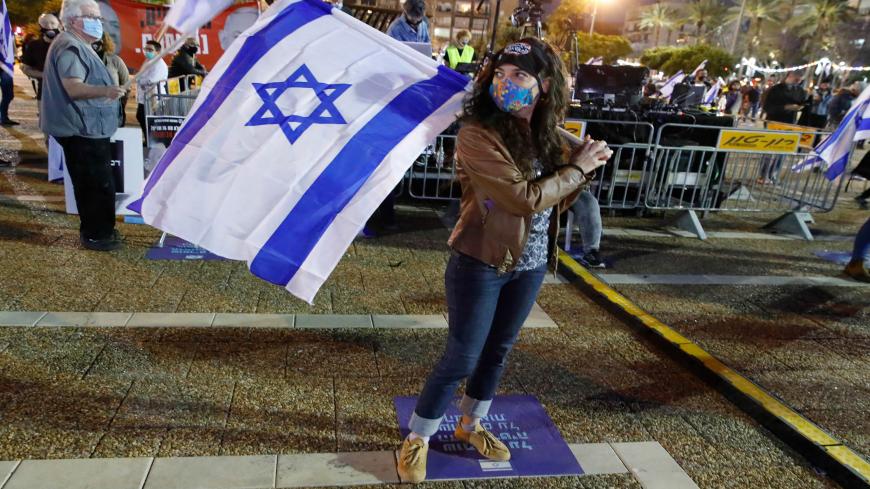 An Israeli woman wearing a protective mask carries a national flag as she takes part in a demonstration in Tel Aviv's Rabin Square on May 2, 2020, in favour of the Supreme Court to consider tomorrow to block the coalition government agreed between Prime Minister Benjamin Netanyahu and his rival-turned-partner Benny Gantz. - If the expanded panel of 11 judges set to hear the case deems the coalition deal invalid, Israel may be forced to hold its fourth election in less than two years. (Photo by JACK GUEZ / A