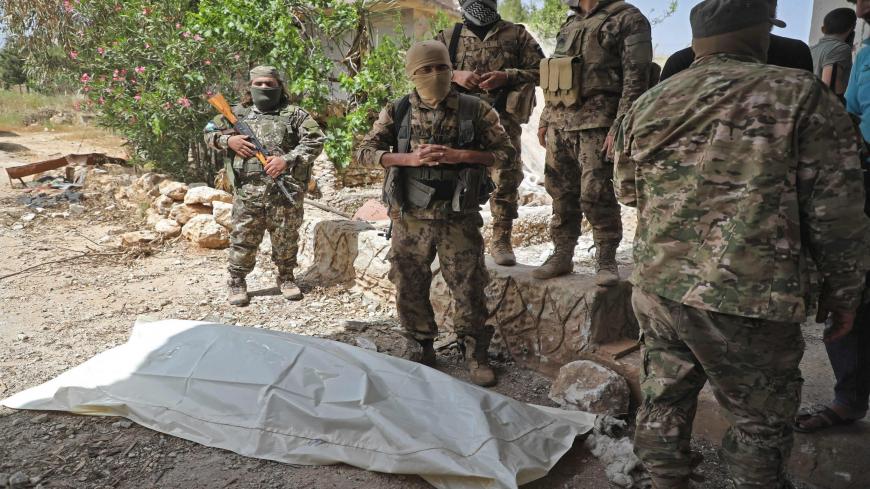 Fighters from the Hayat Tahrir al-Sham group stand over the body of a Syrian regime soldier before the start of a reported prisoner swap deal in the town of Darret Ezza, about 30 kilometres northwest of the northern Syrian city of Aleppo on May 16, 2020. (Photo by AAREF WATAD / AFP) (Photo by AAREF WATAD/AFP via Getty Images)