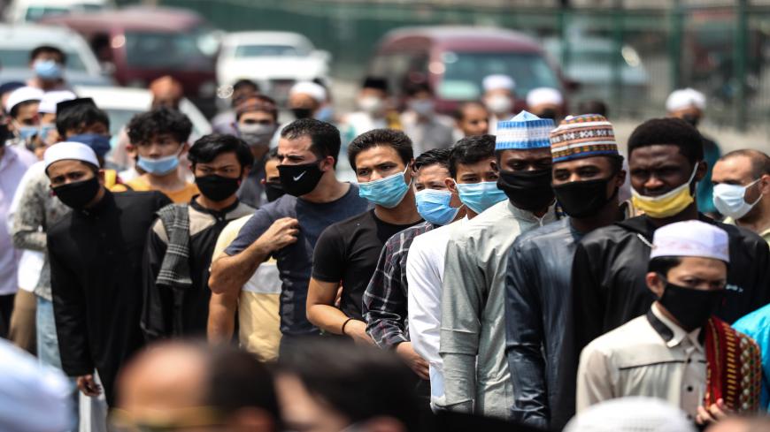 Muslim worshippers, mask-clad due to the COVID-19 coronavirus pandemic, wait outside the historic al-Azhar mosque in the centre of Islamic Cairo as they arrive to perform the Friday prayers under new pandemic restrictions, in Egypt's capital on August 28, 2020. - Egypt allowed Friday prayers to resume in major mosques under strict preventive measures, including mandatory masks for all worshippers, enforcement of social distancing, use of personal prayer rugs, and reduced sermon time at only 10 minutes. (Pho