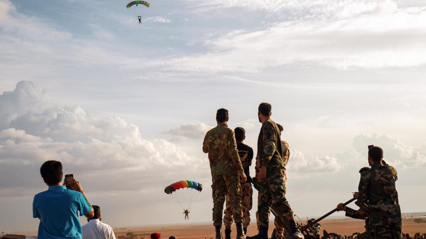 Attendees watch as a paratrooper makes a landing during an event by members of the the "Saiqa" (Special Forces) of the self-proclaimed Libyan National Army (LNA), loyal to eastern strongman Khalifa Haftar, in tribute to the unit's late commander General Wanis Bukhamada, who died a week prior, in the eastern city of Benghazi on November 6, 2020. (Photo by Abdullah DOMA / AFP) (Photo by ABDULLAH DOMA/AFP via Getty Images)