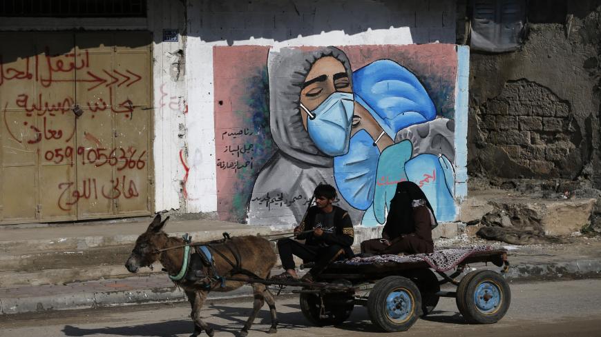 A Palestinian man and his wife ride a donkey cart past street art showing doctors mask-clad due to the COVID-19 coronavirus pandemic in the Nusseirat refugee camp in the central Gaza Strip on November 16, 2020. (Photo by MOHAMMED ABED / AFP) (Photo by MOHAMMED ABED/AFP via Getty Images)