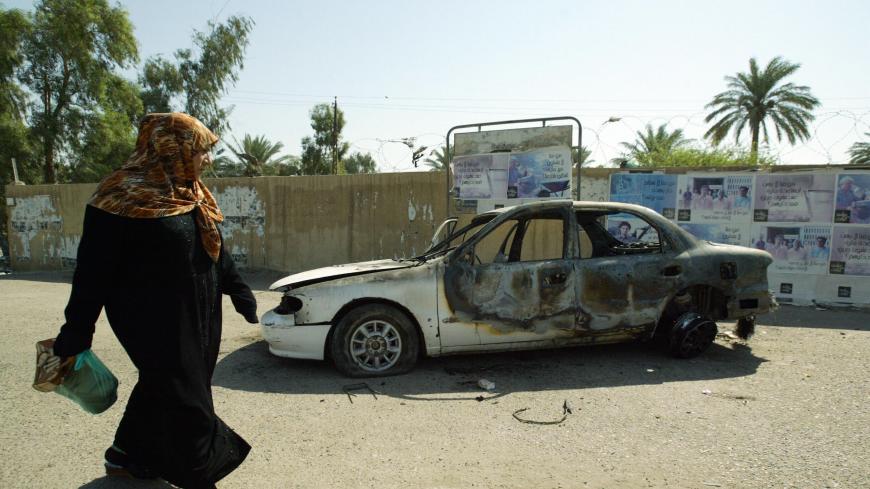 An Iraqi woman walks past 24 September 2007, at a burnt car on the site where Blackwater guards who were escorting US embassy officials opened fire in the western Baghdad neighbourhood of Yarmukh, a shootout which left, 16 September 2007, nine civilians and a policeman dead. Iraq said today that it will await the outcome of an investigation into the killing of 10 people during the shootout before taking any action against the company. AFP PHOTO/ALI YUSSEF (Photo credit should read ALI YUSSEF/AFP via Getty I