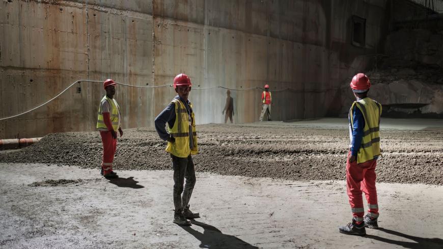 Construction workers stand at the construction site at the Grand Ethiopian Renaissance Dam (GERD),  near Guba in Ethiopia, on December 26, 2019. - The Grand Ethiopian Renaissance Dam, a 145-metre-high, 1.8-kilometre-long concrete colossus is set to become the largest hydropower plant in Africa.
Across Ethiopia, poor farmers and rich businessmen alike eagerly await the more than 6,000 megawatts of electricity officials say it will ultimately provide. 
Yet as thousands of workers toil day and night to finish 