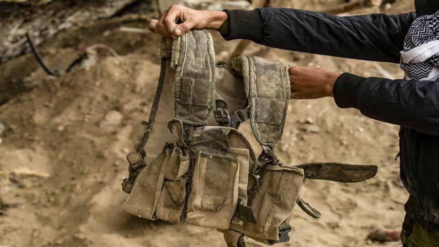 A fighter from the Syrian Democratic forces (SDF) carries a military vest said to have belonged to Islamic State (IS) group jihadists, recovered in the eastern Syrian village of Baghuz on March 13, 2020, a year after the fall of the Islamic State's (IS) caliphate. - A year after the last black flag of the Islamic State group was lowered in the Syrian village of Baghouz, traces of the jihadist group are still all around this small and remote village near the Iraqi border, where Kurdish fighters and the US-le