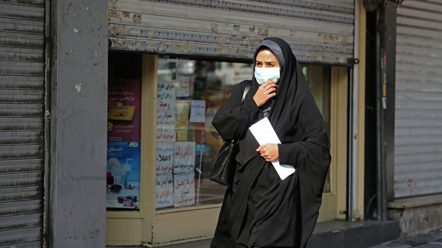 A woman wearing a face mask amid the COVID-19 pandemic walks by closed shops in the Iranian capital Tehran, on November 30, 2020. (Photo by ATTA KENARE / AFP) (Photo by ATTA KENARE/AFP via Getty Images)