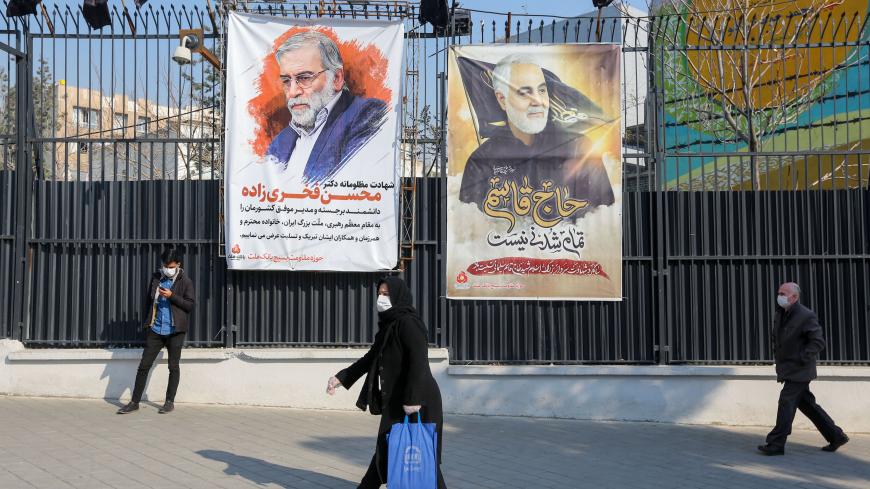 Iranians walk past a poster depicting late Revolutionary Guards commander Qasem Soleimani (R) and nuclear scientist Mohsen Fakhrizadeh, assassinated last month, in the capital Tehran, on December 30, 2020. - On January 3, Iraq will mark a year since a US drone strike killed Soleimani, head of the elite external operations of Iran's Revolutionary Guards, alongside Abu Mahdi al-Muhandis, the deputy head of Iraq's powerful Tehran-aligned Hashed Al-Shaabi paramilitary network, nearly sparking a conflict that ma