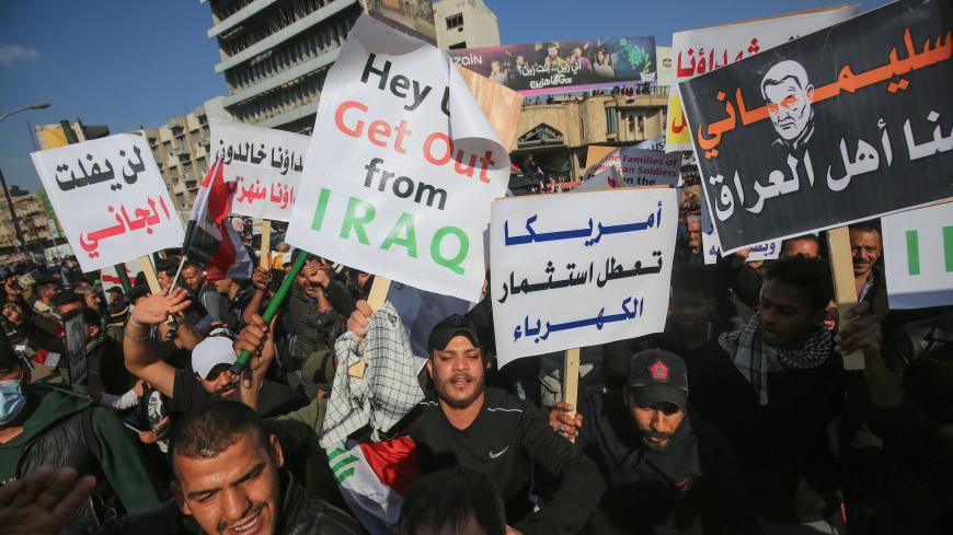 Iraqi demonstrators lift anti-US placards during a rally marking the first anniversary of the killing of Iraqi commander Abu Mahdi al-Muhandis (L) and Iranian Revolutionary Guards commander Qasem Soleimani, in Tahrir square in the capital Baghdad on January 3, 2021. - Thousands of Iraqi mourners chanted "revenge" and "no to America", one year after the US strike which killed Soleimani and al-Muhandis and brought Washington and Tehran to the brink of war in early 2020, an anniversary that was also marked in 