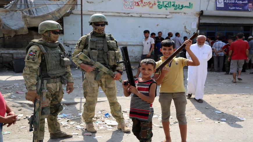 TOPSHOT - A picture taken during a press tour provided by the Russian Armed Forces on September 15, 2017 shows Russian soldiers standing guard in a central street in Syria's eastern city of Deir Ezzor, as local children pose nearby. / AFP PHOTO / France2 / Dominique DERDA        (Photo credit should read DOMINIQUE DERDA/AFP via Getty Images)