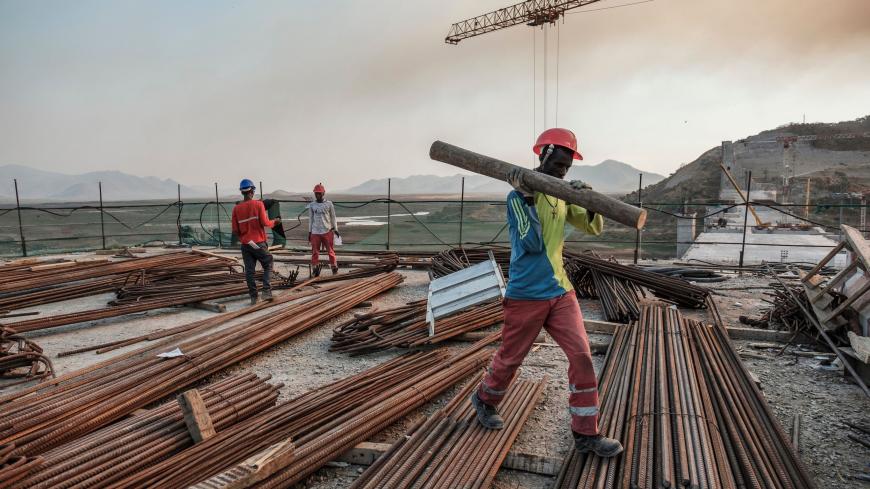 A worker walks with a piece of wood on his shoulder at the Grand Ethiopian Renaissance Dam (GERD),  near Guba in Ethiopia, on December 26, 2019. - The Grand Ethiopian Renaissance Dam, a 145-metre-high, 1.8-kilometre-long concrete colossus is set to become the largest hydropower plant in Africa.
Across Ethiopia, poor farmers and rich businessmen alike eagerly await the more than 6,000 megawatts of electricity officials say it will ultimately provide. 
Yet as thousands of workers toil day and night to finish 