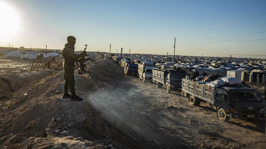 TOPSHOT - A masked guard keeps watch as trucks transports Syrians leaving the Kurdish-run al-Hol camp holding relatives of alleged Islamic State (IS) group fighters, in the al-Hasakeh governorate in northeastern Syria, on November 24, 2020. - A Kurdish official in charge of the region's camps, said 515 people from 120 families were returning to areas in the east of Deir Ezzor province, the first to do so after the Kurdish authorities in northeast Syria vowed to allow thousands of Syrians including the famil
