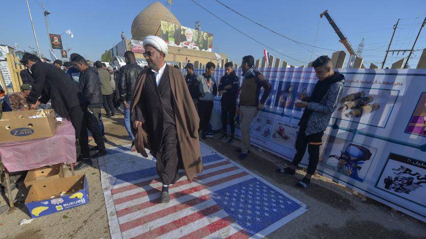 An Iraqi cleric walks on a US flag painted on the ground as people gather to pay respects by the grave of slain commander Abu Mahdi al-Muhandis at the Wadi al-Salam ("Valley of Peace") cemetery in the holy city of Najaf, on January 4, 2021, marking the first anniversary of his killing alongside Iranian Revolutionary Guards commander Qasem Soleimani in a US drone strike. (Photo by Ali NAJAFI / AFP) (Photo by ALI NAJAFI/AFP via Getty Images)