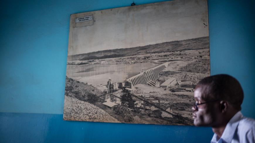 A man sits next to an old picture of the Inga hydroelectric dam displayed on the wall of the Societe Nationale d'Electricite (SNEL, National Electricity Company) offices in Lubumbashi on May 27, 2015. AFP PHOTO / FEDERICO SCOPPA        (Photo credit should read FEDERICO SCOPPA/AFP via Getty Images)