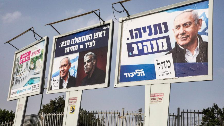 A man walks past election billboards of the Israeli Likud party (R to L) showing the face of Prime Minister and Likud leader Benjamin Netanyahu with the tagline "leader", and another showing Netanyahu with political opponent Yair Lapid with text in Hebrew reading "the next prime minister: Lapid or Netanyahu", in the southern Israeli city of Beersheba on March 15, 2021, ahead of the election due later in the month. (Photo by HAZEM BADER / AFP) (Photo by HAZEM BADER/AFP via Getty Images)