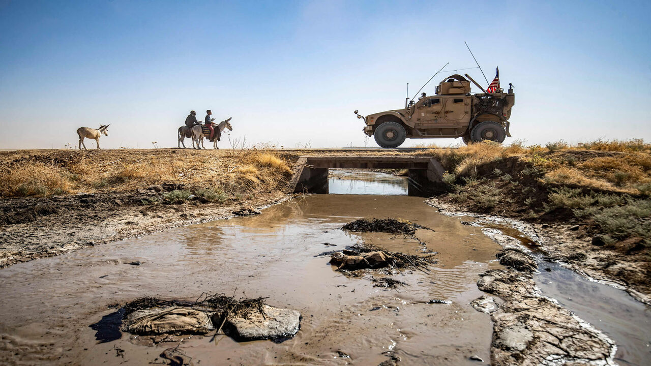 Youths ride donkeys near a US military vehicle crossing a stream polluted by an oil spill near the village of Sukayriyah, in the countryside south of Rumaylan (Rmeilan) in the Kurdish-controlled northeastern Hasakeh province, Syria, July 19, 2020.