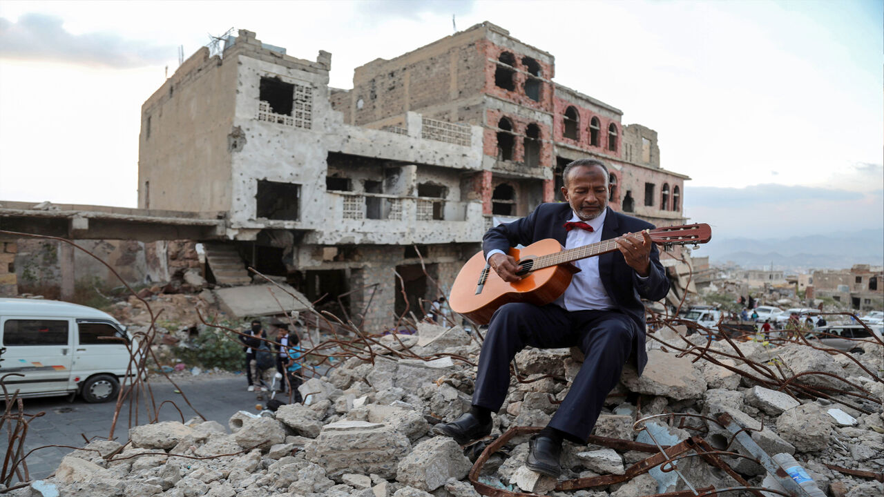 A Yemeni artist sitting atop the rubble of a collapsed buiding plays the guitar during a street performance, Taez, Yemen, Dec. 6, 2019.