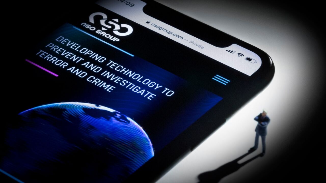 A studio photographic illustration shows the website of NSO Group on a phone -- court documents suggested creditors sought to push the firm to continue selling Pegasus spyware to countries with questionable rights records