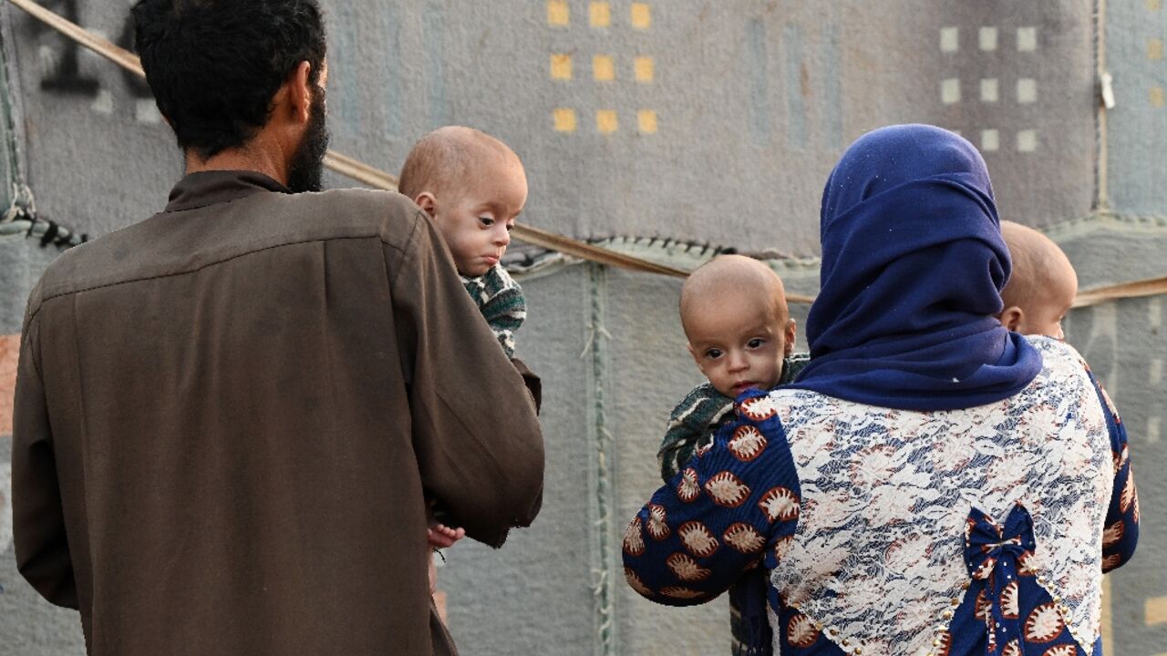 A man and woman carry malnourished children at a camp for Syrians displaced by conflict in Aleppo province on September 28, 2020