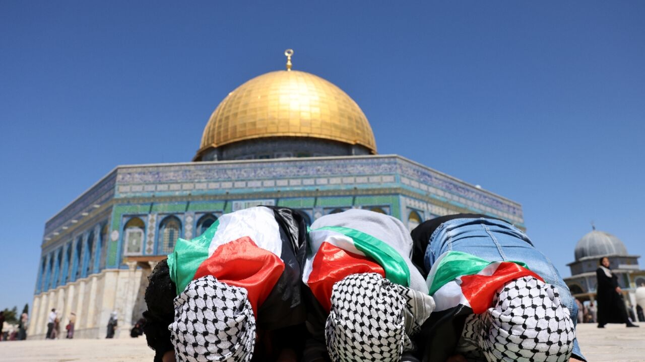 Palestinian girls, wearing the Palestinian flag, pray in front of the Dome of Rock mosque at the Al-Aqsa mosque compound in Jerusalem's Old City on April 15, 2022