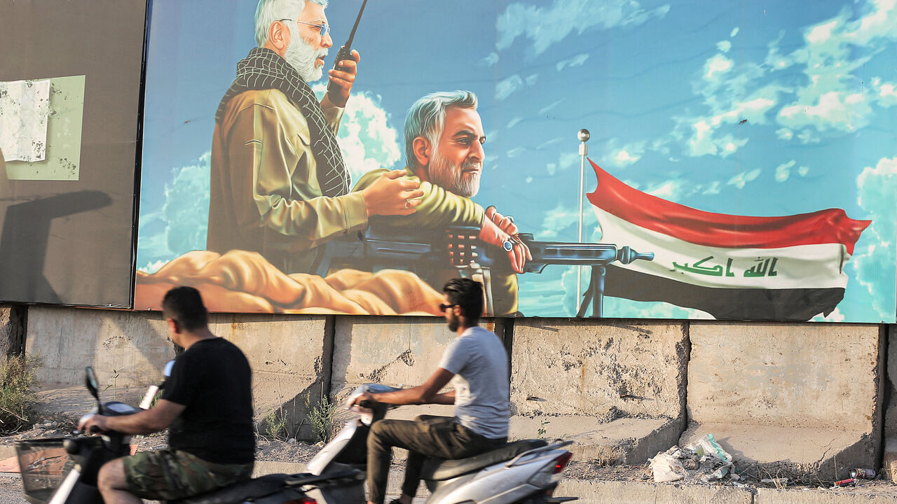 Men ride scooters past a billboard depicting (L to R) the late commander of the Popular Mobilization Units Abu Mahdi al-Muhandis and Iran's Islamic Revolutionary Guard Corps commander Qassem Soleimani, Baghdad, Iraq, June 13, 2021.