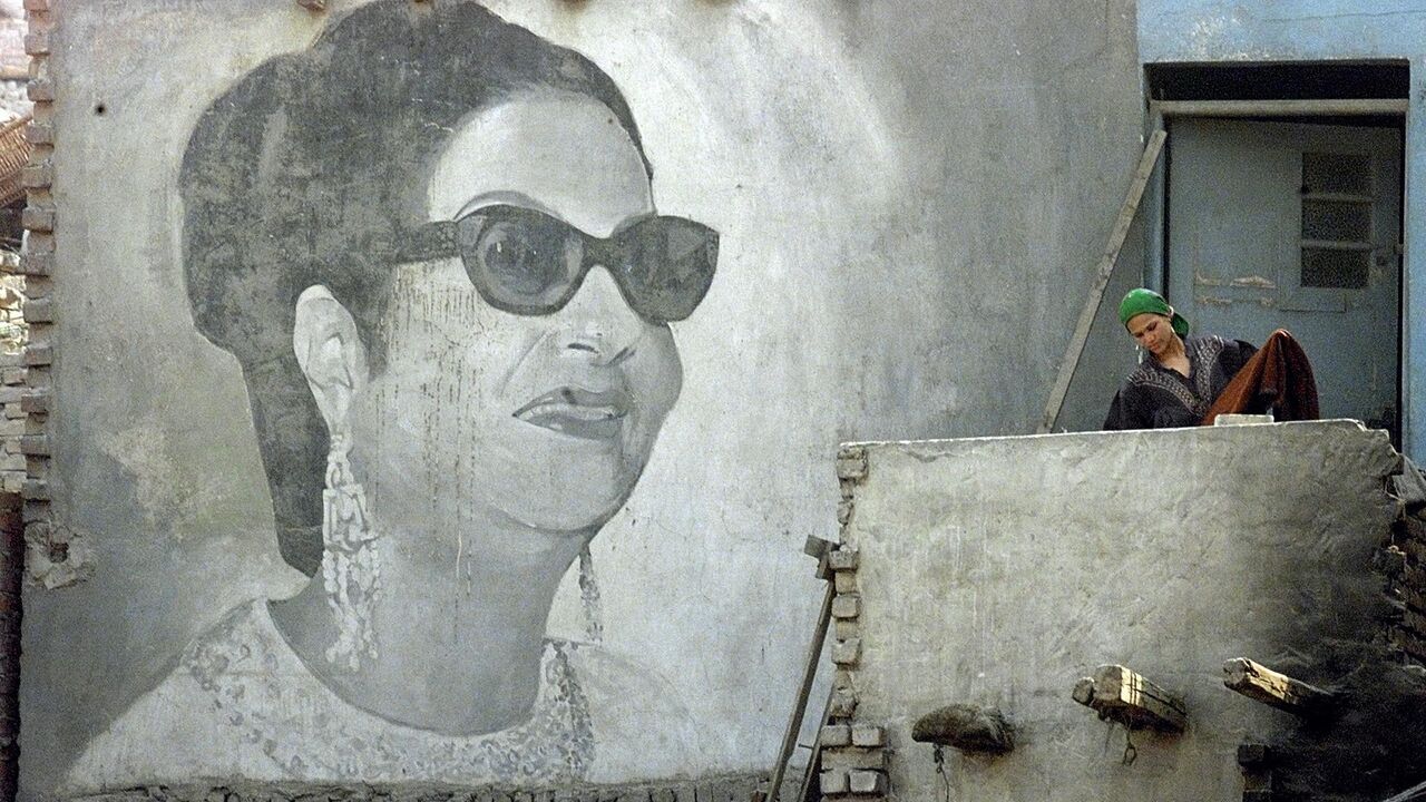 An Egyptian woman collects clothes in front of a giant picture of Egyptian diva Umm Kulthum painted on her shack in the Kom al-Ghurab suburb of Cairo. (MARWAN NAAMANI/AFP via Getty Images)