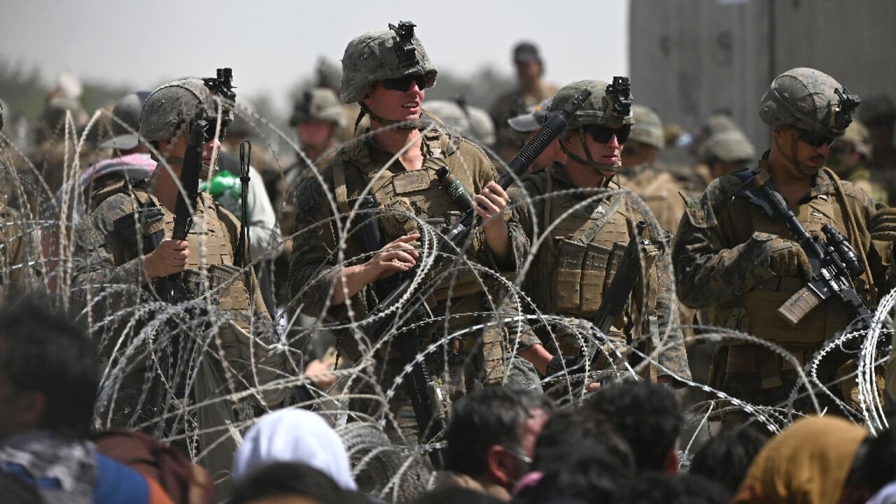 US soldiers stand guard behind barbed wire as Afghans sit on a roadside near the military part of the airport in Kabul on August 20, 2021, hoping to flee from the country after the Taliban's military takeover of Afghanistan