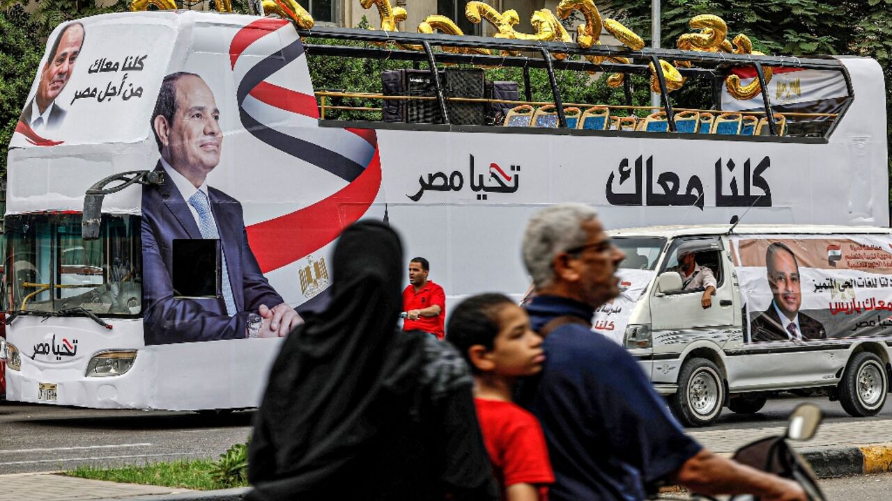 A man, child, and woman ride a motorcycle across the street from an election campaign bus for Egypt's President Abdel Fattah al-Sisi adorned with his image and slogan "Long Live Egypt"