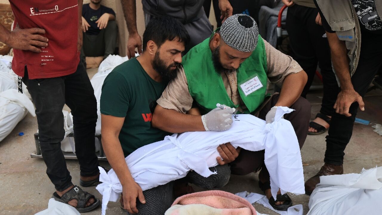 A man writes the name on the shroud of a child killed in an Israeli strike on Deir Balah in central Gaza
