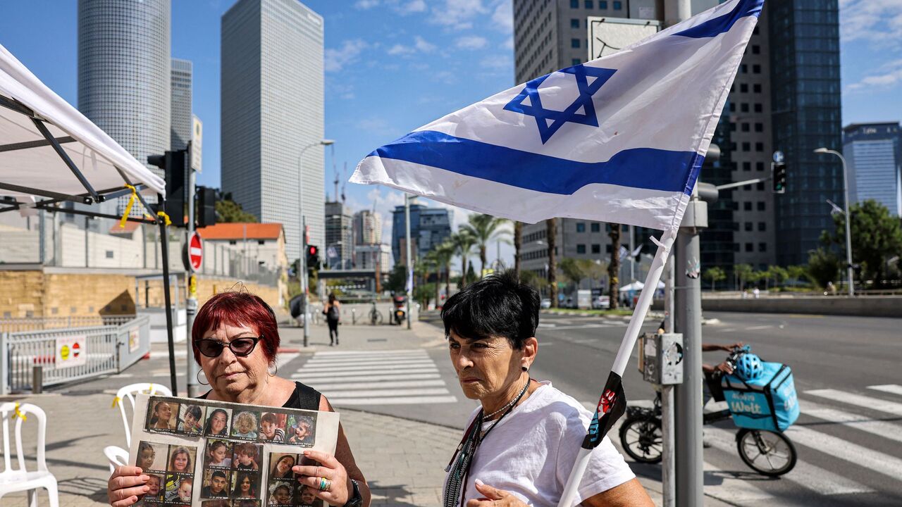 An elderly woman stands with an Israeli flag next to another holding a sign showing the faces of young Israeli hostages held by Palestinian militants since the October 7 attack near Azrieli Mall in Tel Aviv on October 18, 2023. (Photo by AHMAD GHARABLI / AFP) (Photo by AHMAD GHARABLI/AFP via Getty Images)