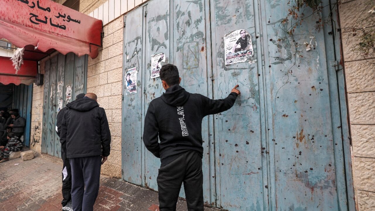 Palestinians inspect the bullet holes in the shutters of a shop in the West Bank town of Azzun after Israeli troops carried out a deadly raid