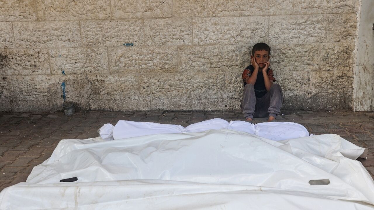 A child sits beside the shrouded corpses of people killed in an overnight Israeli strike, in the yard of the Al-Aqsa Martyrs hospital in Deir el-Balah in the central Gaza Strip