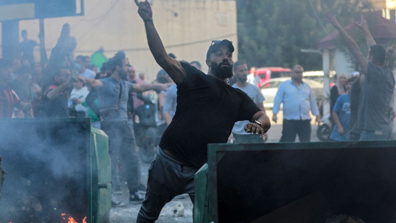 A man throws a stone from behind a burning rubbish container as displaced people who fled Israeli bombardment in Beirut's southern suburbs clash with Lebanese security forces in central Beirut