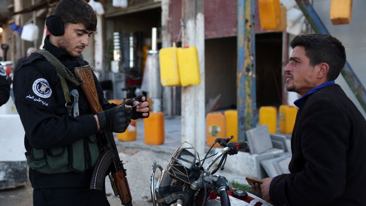 Security forces under Syria's new authorities check the identification of a man in Homs