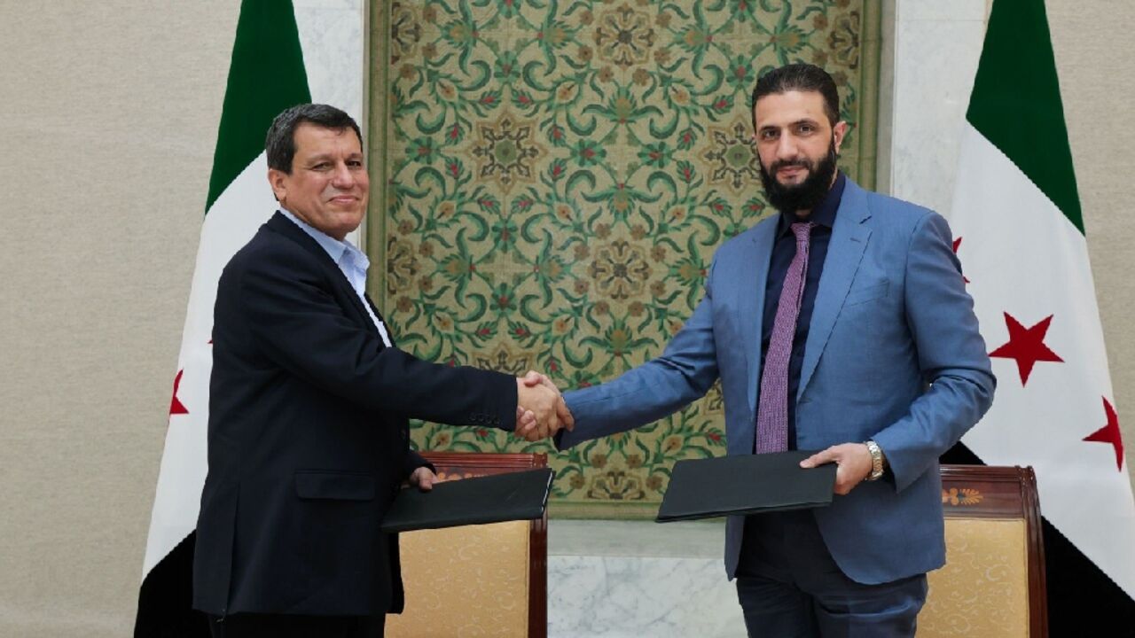 Syrian interim president Ahmed al-Sharaa (R) shakes hands with Syrian Democratic Forces (SDF) head Mazloum Abdi after signing an agreement in Damascus